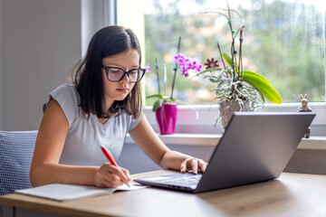 Young girl writing in notebook. Woman studying at home with laptop. Hand of schoolgirl with pen and copybook at desk. Businesswoman at homework