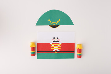 Flat lay of nutcracker soldier paper cutout parts with cardboard roll, glue stick and scissors,...