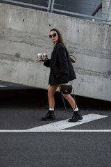Fashionable urban lifestyle – young woman with coffee-to-go, chic black outfit and bold...