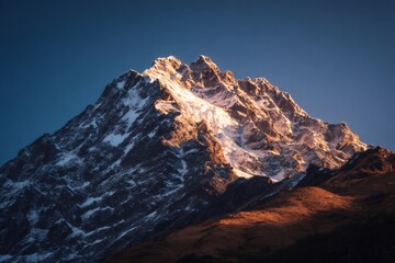 Obraz premium Warm sunlight illuminating snowy mountain peak against clear blue sky, creating breathtaking scenery