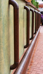 Brown metal railing with curved metal supports against a textured green wall, creating a rustic...
