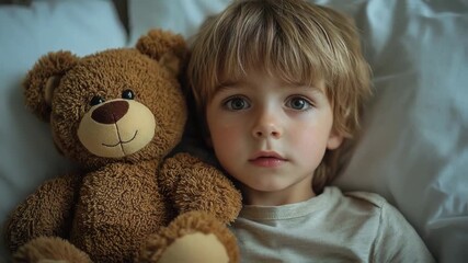 A young child with a teddy bear lies on a bed, gazing thoughtfully, with soft lighting