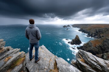 Man on cliff overlooking stormy ocean and rocky coast