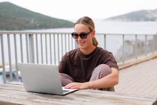 Young woman working remotely by the sea with a laptop and solar panel, embracing sustainable travel, mindful lifestyle and digital freedom. Concept of new work, balance and conscious living.