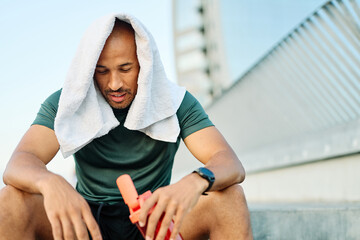 Portrait of a young man holding a bottle of water refreshment tired after exercicing outdoors. Athlete and fitness and healhty living concept