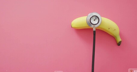 Pressing stethoscope chestpiece and tubing against ripe yellow banana on pink tabletop, copy space