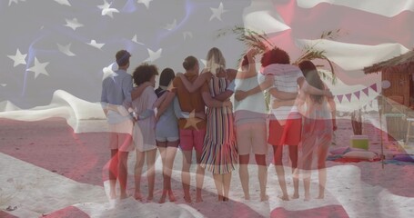 Leaning friends placing arms around shoulders on sandy shoreline, with hut bunting flags cushions
