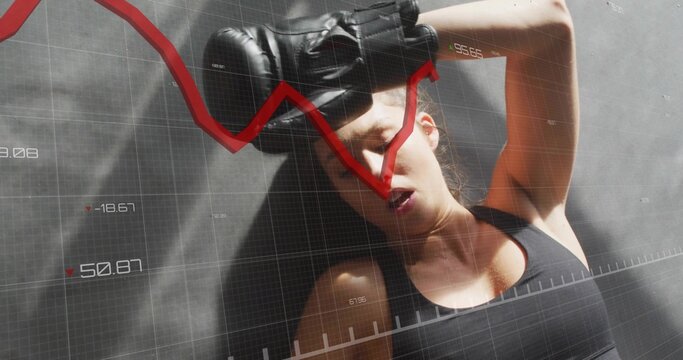 Punching fit woman wearing black sports top and boxing gloves in gym, with data overlay