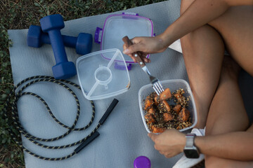 Muscular athlete consuming protein-rich meal while seated on yoga mat, surrounded by workout equipment like dumbbells and jump rope, representing dedicated fitness lifestyle