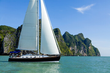 Sailboat sailing through Phang Nga Bay near Phuket, Thailand on a sunny day.