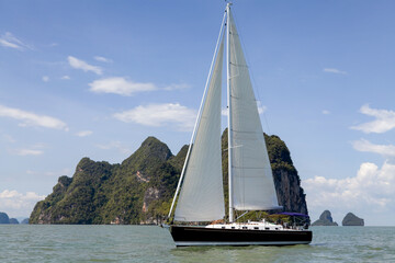 Sailboat sailing through Phang Nga Bay near Phuket, Thailand on a sunny day.