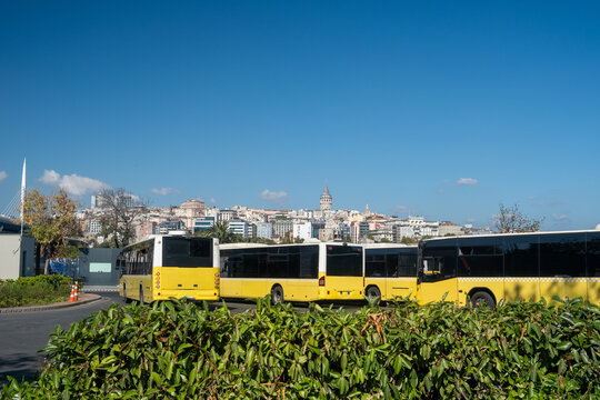 Yellow public buses at Unkapanı bus station with Galata Tower and Beyoğlu district skyline, Istanbul public transportation hub under clear blue sky, Turkey