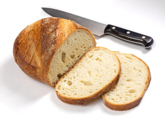 A loaf of sliced white crusty bread with a large sharp kitchen knife isolated on white