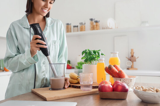 Young woman with hand blender making smoothie for breakfast in kitchen, closeup - Powered by Adobe