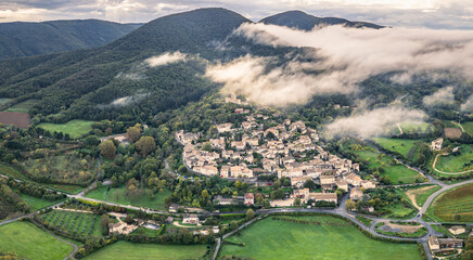 Aerial view of Mirmande village in France with morning fog over hills – picturesque medieval town surrounded by lush green forest and countryside landscape, historic architecture under soft misty sky