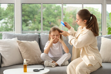 Mother combing her little daughter's hair with pediculosis on sofa at home