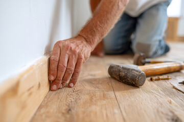 Man installing wooden baseboard in a home renovation project around midday