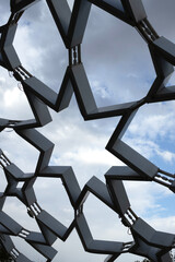 Abstract star-shaped metal lattice roof against a cloudy sky. Modern architectural structure with...