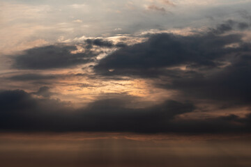 Sunset sky with soft clouds and sun partially hidden behind darker clouds casting warm evening light
