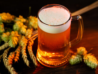 Beer mug on wooden table with hop cones and wheat ears