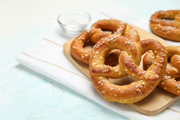 Cutting board with tasty pretzels on blue grunge background, closeup