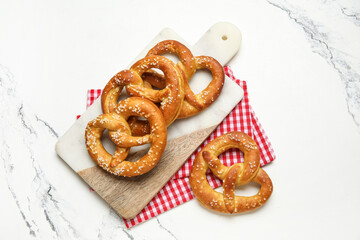 Cutting board with tasty pretzels on marble background, closeup