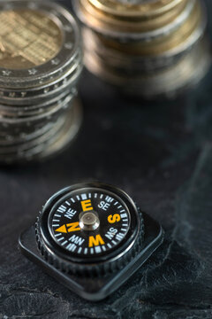 Macro shot of compass on black stone surface texture against euro coin money. Financial market orientation.