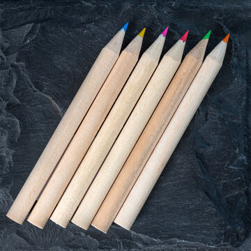 Group of colored pencils on textured dark surface, top view