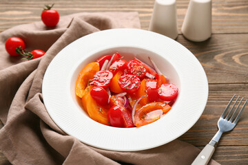 Plate of fresh tomato salad with red onion on wooden background, closeup