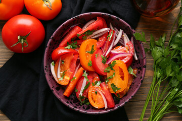 Bowl of fresh tomato salad with red onion and parsley on wooden background
