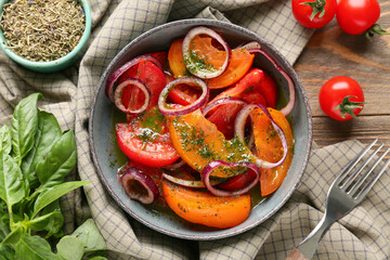 Bowl of fresh tomato salad with red onion and basil leaves on wooden background