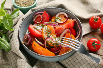 Bowl of fresh tomato salad with red onion and basil leaves on wooden background, closeup