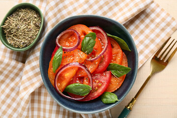 Bowl of fresh tomato salad with red onion and basil leaves on beige wooden background