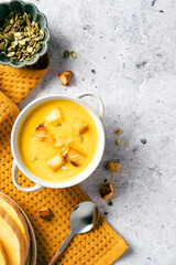 Pumpkin soup with croutons and seeds in handled bowl on mustard textile, served with fresh squash, bread, and seeds, perfect for autumn