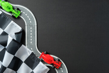 Toy race track puzzle with red and green cars and checkered flag on black background, symbolizing speed, competition, and victory in creative racing concept.
