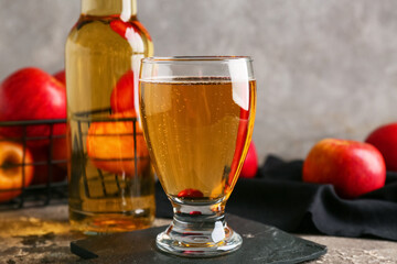 Glass and bottle of fresh apple cider with fruits on grey background