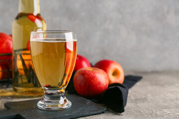 Glass and bottle of fresh apple cider with fruits on grey background