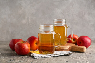 Mason jars of fresh apple cider and fruits on grey background