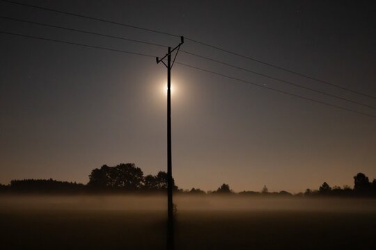 Power pole silhouette with moonlight and misty night landscape, mysterious rural scenery under dark sky - Powered by Adobe