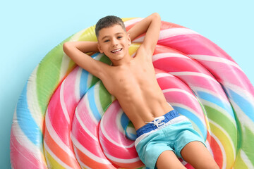 Cute little boy lying on inflatable mattress against blue background