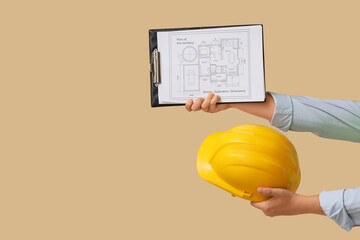 Male hands holding hardhat and building plan on beige background
