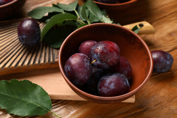 Bowl with fresh ripe plums on wooden background, closeup
