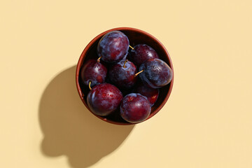 Bowl with fresh ripe plums on yellow background