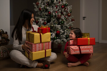 Mother and daughter holding christmas gifts near christmas tree
