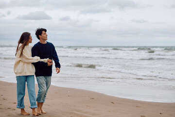 Romantic couple enjoying a relaxing walk on the beach, holding hands and looking out at the ocean