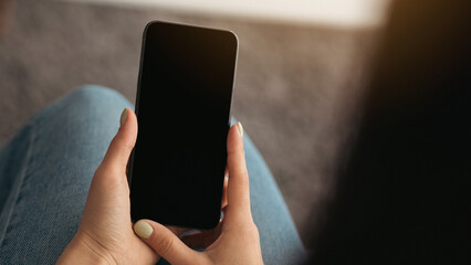Online ad, offer, app, website for remote communication and work during social distancing. Millennial lady holds smartphone with empty screen, in living room interior, view from over shoulder, cropped