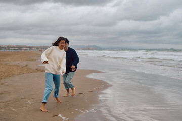 Young couple running barefoot along the beach, laughing and enjoying each other's company on a...