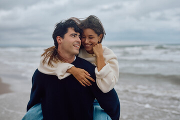 Young man giving piggyback ride to his girlfriend on the beach, enjoying a romantic day together