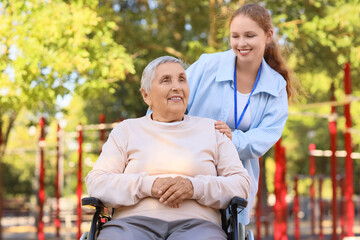 Fototapeta premium Young caregiver with senior woman in wheelchair outdoors