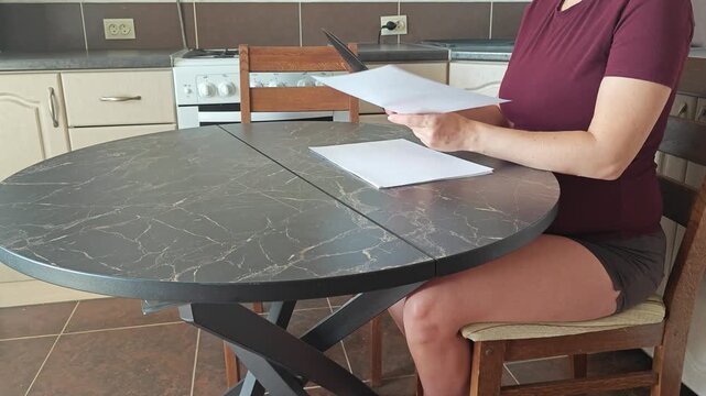 A girl at the kitchen table cuts white paper with scissors